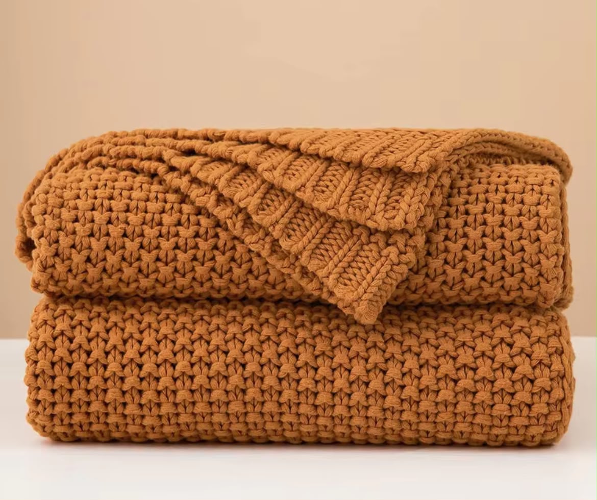 Chunky knit throw blanket beige cream folded on white surface