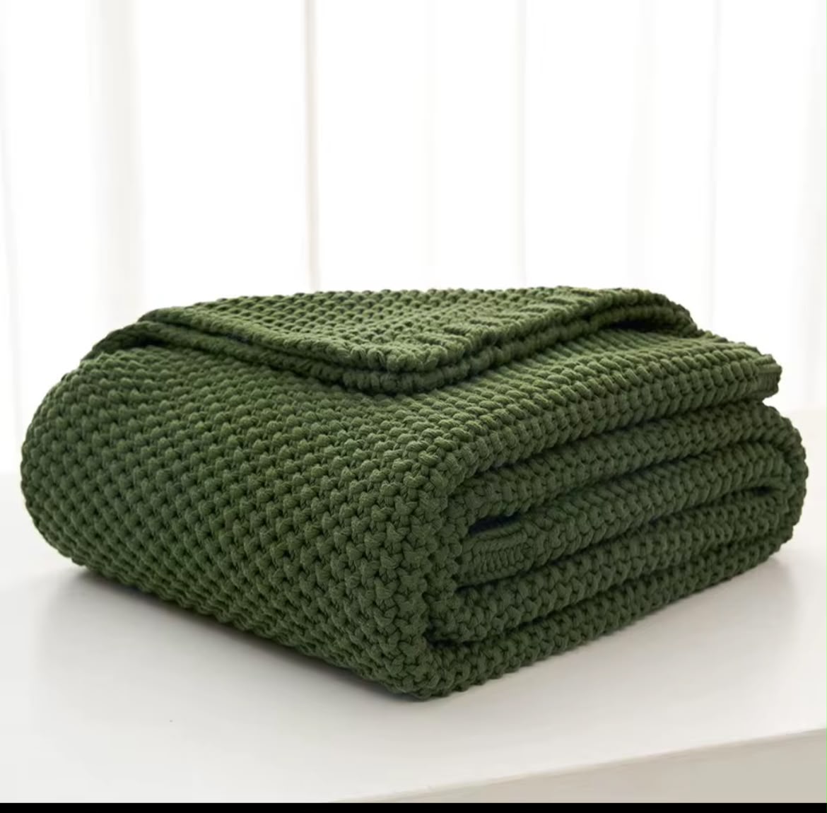 Chunky knit throw blanket burgundy red folded on white surface
