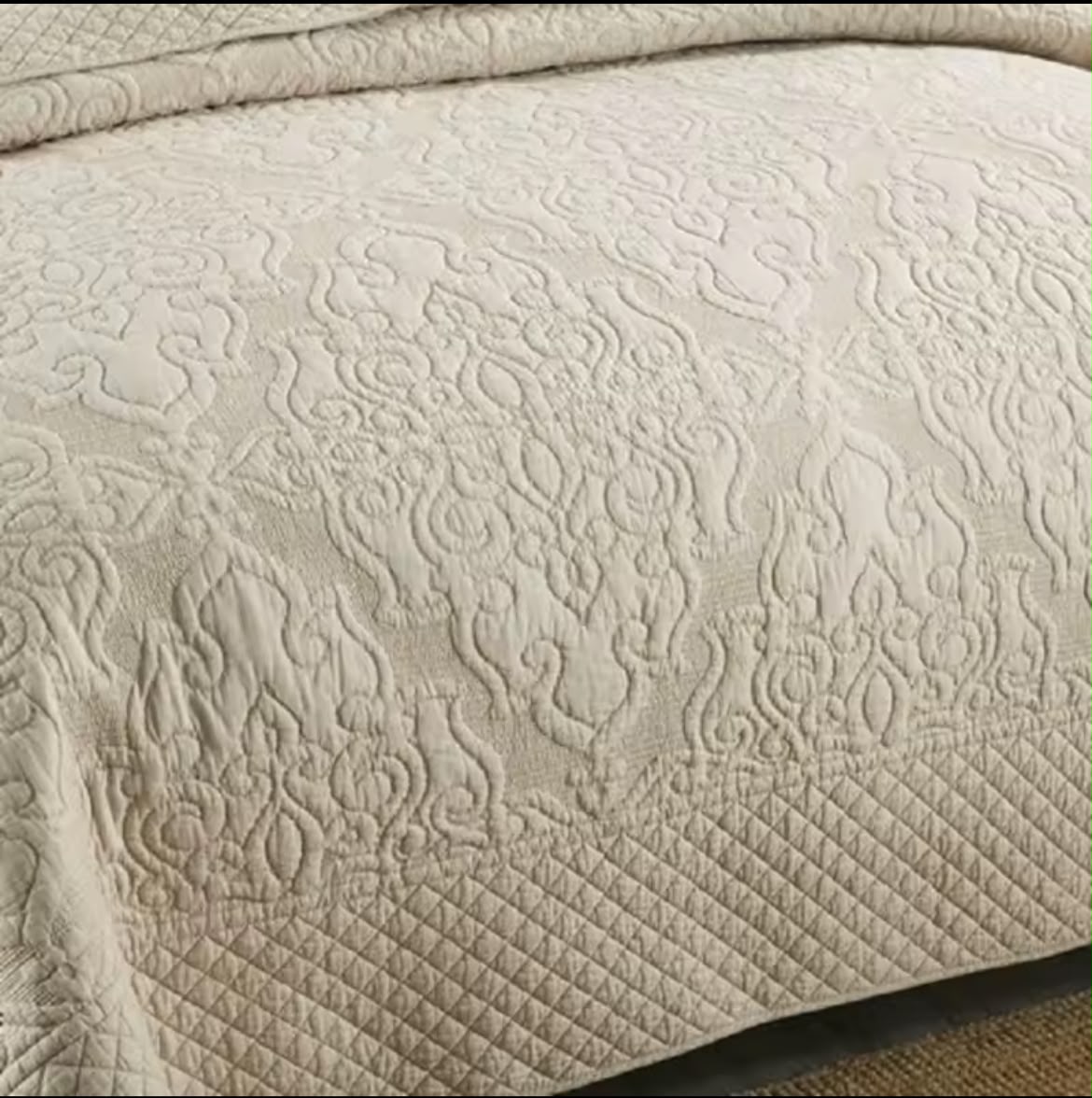 Corner detail of natural cotton quilt showing arabesque embroidery pattern over bed edge