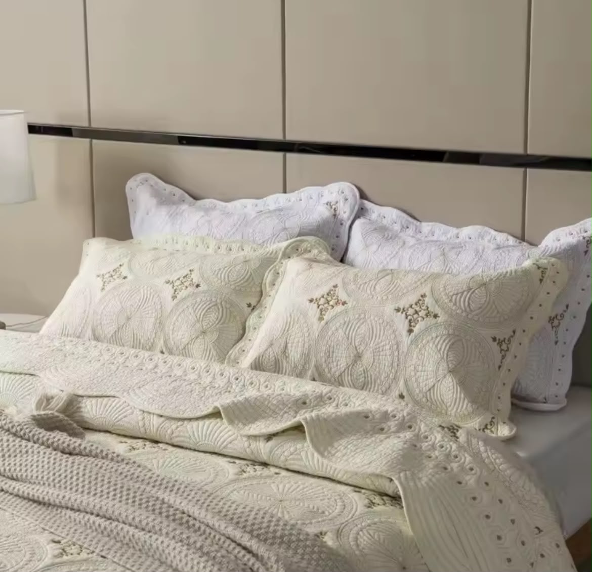 White embroidered quilted pillowcases stacked on bed with gold lamp luxury bedroom
